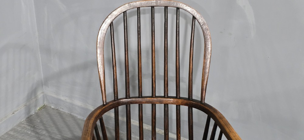 An antique dark brown timber Windsor armchair featuring a high hoop spindle back, curved armrests with turned supports, and a shaped solid wooden seat. View VI