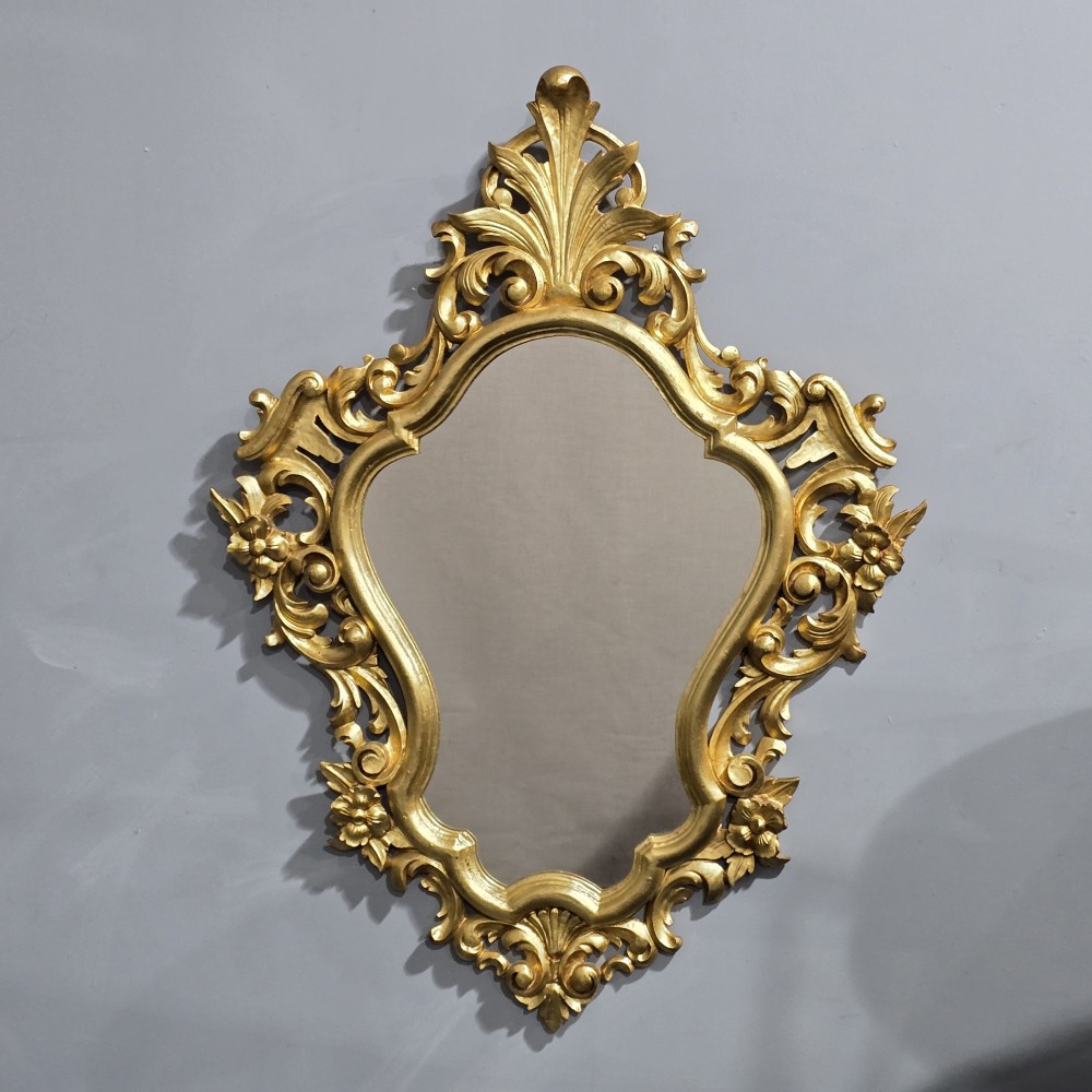 An ornate Venetian giltwood wall mirror featuring a carved foliate cresting, scrolling acanthus leaf motifs, and a shaped glass plate.