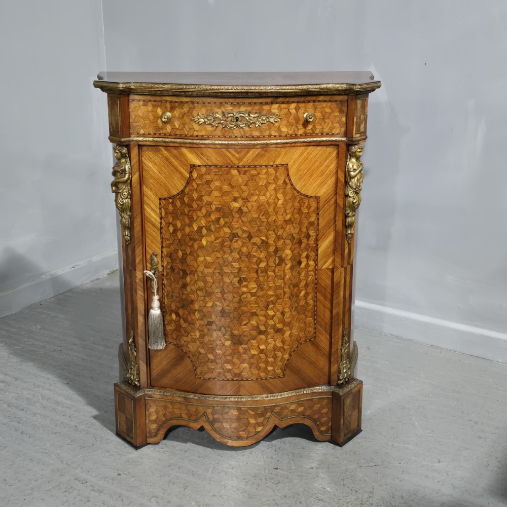 A French Louis XV style serpentine side cabinet featuring geometric cubework parquetry inlay, a single door, and decorative gilt-bronze mounts.