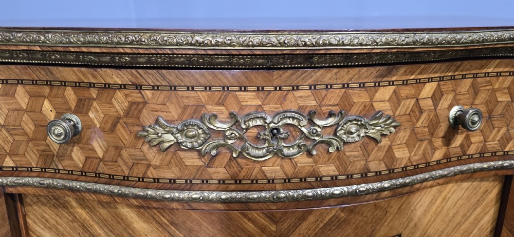 A French Louis XV style serpentine side cabinet featuring geometric cubework parquetry inlay, a single door, and decorative gilt-bronze mounts. View XVI