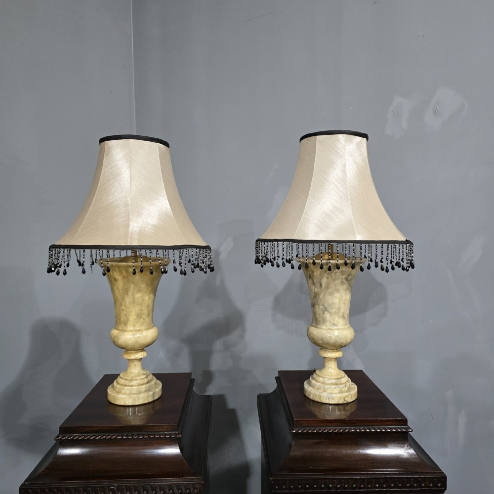 A pair of carved cream Italian marble urn-form table lamps with fabric shades trimmed in dark beaded fringe.