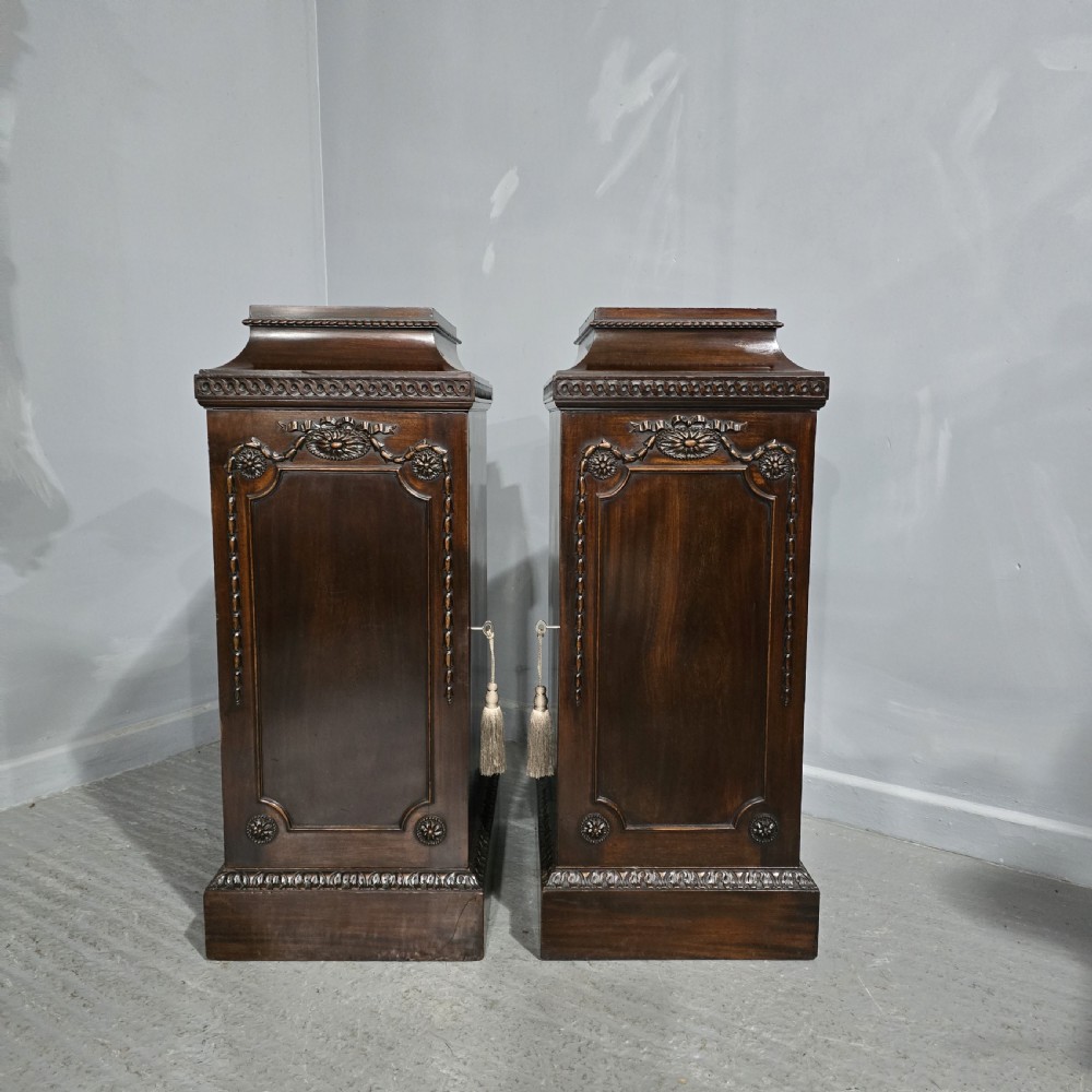 A pair of dark mahogany Regency style side cabinets featuring carved swags, floral rosettes, stepped tops, and plinth bases.