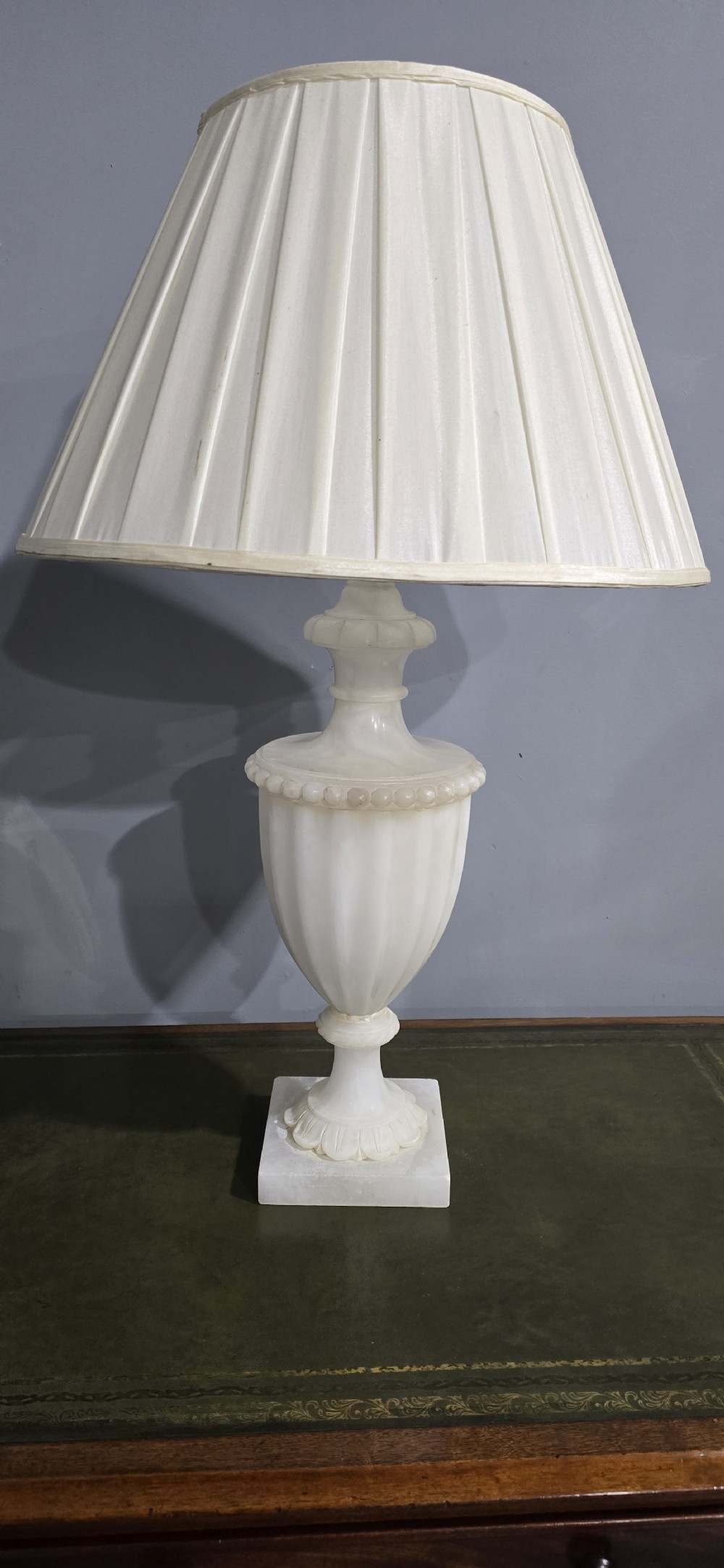 A carved off-white alabaster urn-shaped table lamp on a square pedestal base, fitted with a pleated cream fabric shade. View II