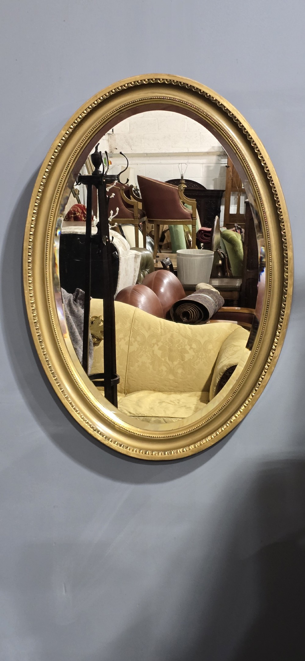 An oval wall mirror framed in a gold gilt moulded rim with beaded detailing. View II