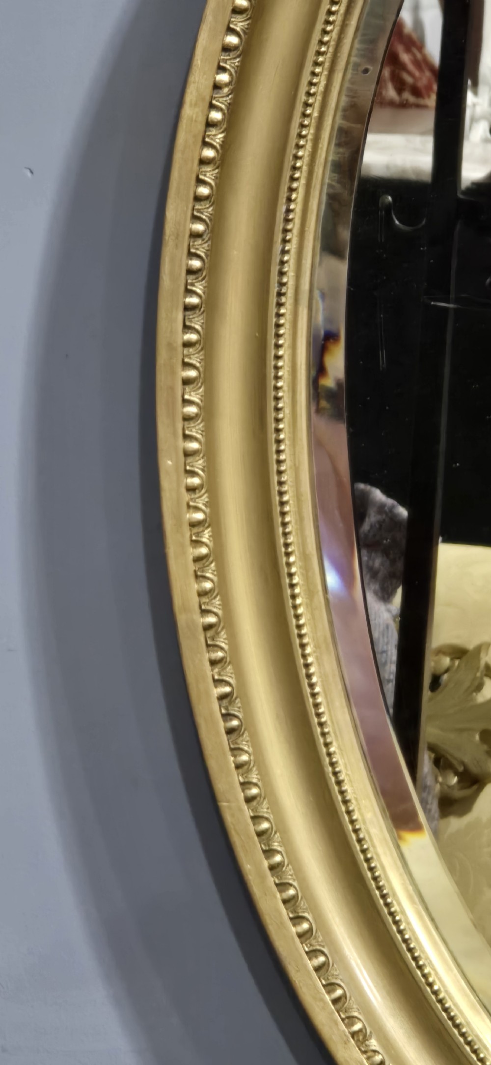 An oval wall mirror framed in a gold gilt moulded rim with beaded detailing. View III