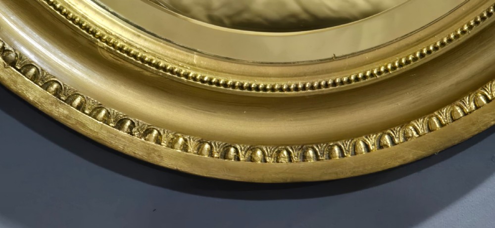 An oval wall mirror framed in a gold gilt moulded rim with beaded detailing. View IV
