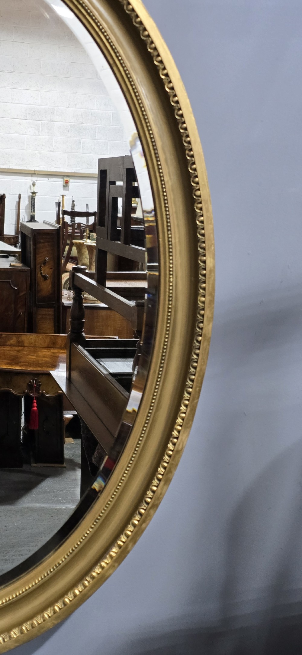 An oval wall mirror framed in a gold gilt moulded rim with beaded detailing. View V