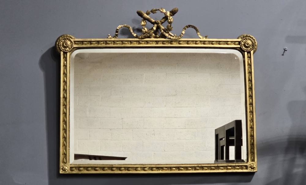 A rectangular Victorian giltwood wall mirror featuring a crested top with ribbon motifs and carved rosettes at the upper corners. View II