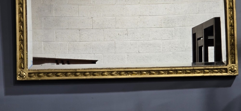 A rectangular Victorian giltwood wall mirror featuring a crested top with ribbon motifs and carved rosettes at the upper corners. View V