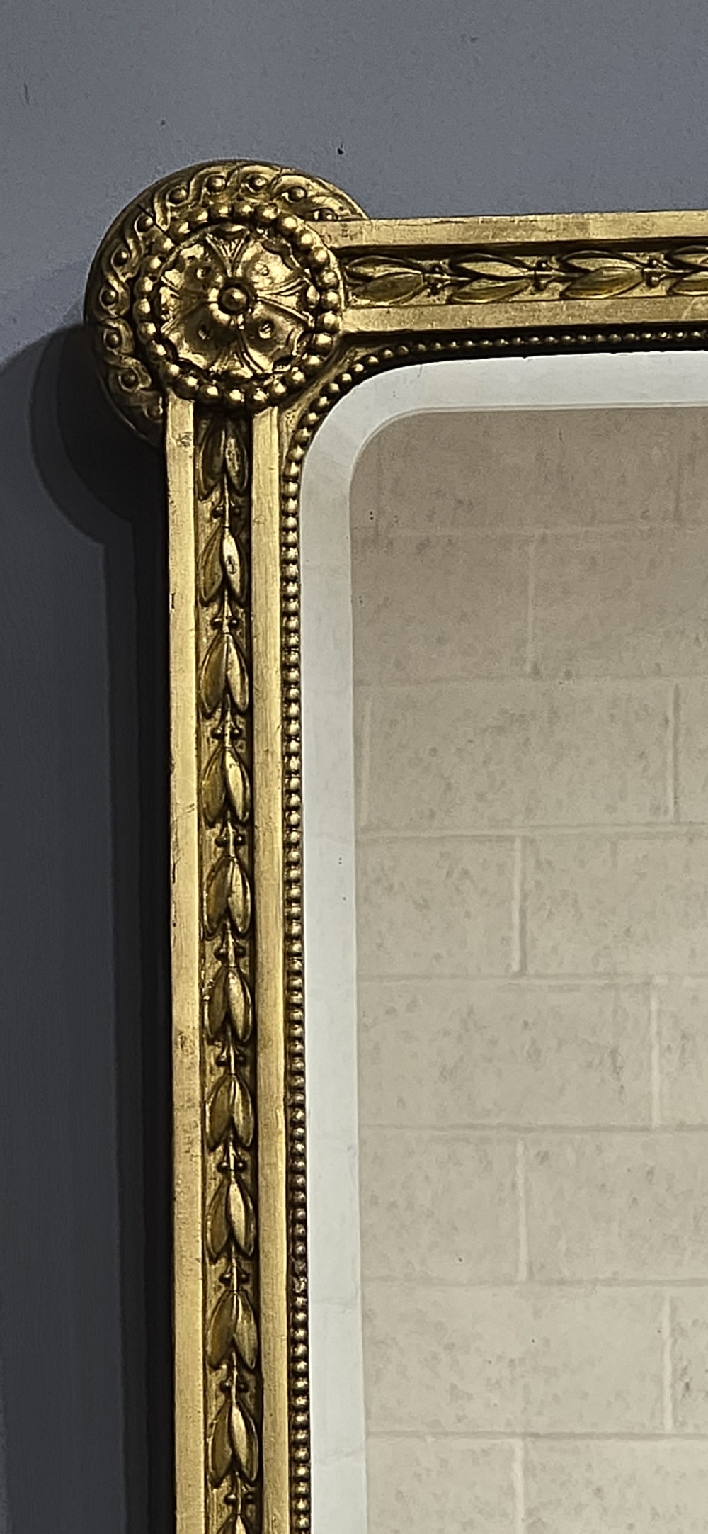 A rectangular Victorian giltwood wall mirror featuring a crested top with ribbon motifs and carved rosettes at the upper corners. View VIII