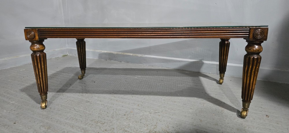 A low rectangular mahogany coffee table featuring a glass-covered woven cane top, reeded frieze, carved corner rosettes, and tapered reeded legs terminating in brass castors. View II