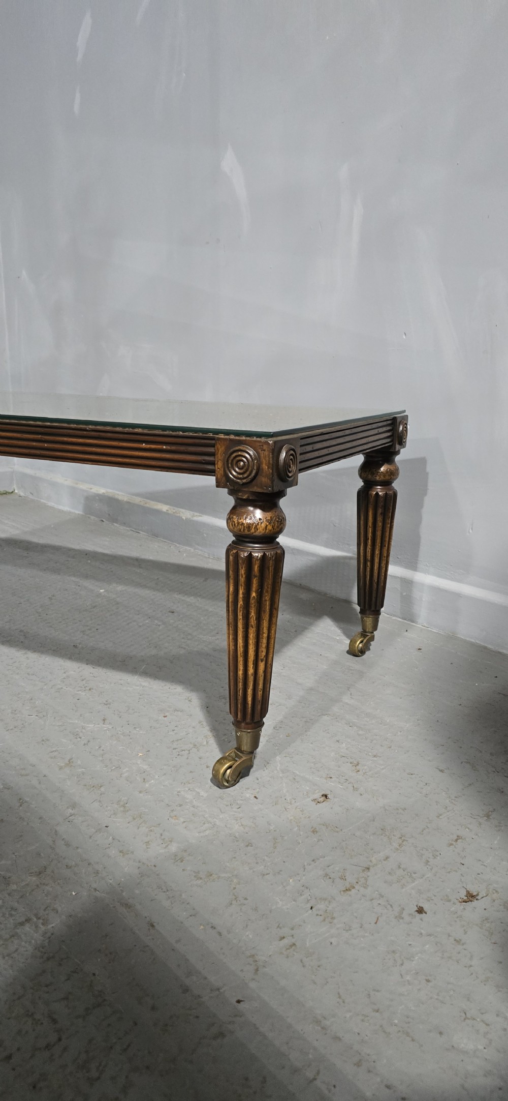 A low rectangular mahogany coffee table featuring a glass-covered woven cane top, reeded frieze, carved corner rosettes, and tapered reeded legs terminating in brass castors. View III
