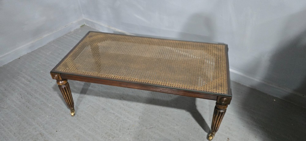 A low rectangular mahogany coffee table featuring a glass-covered woven cane top, reeded frieze, carved corner rosettes, and tapered reeded legs terminating in brass castors. View V