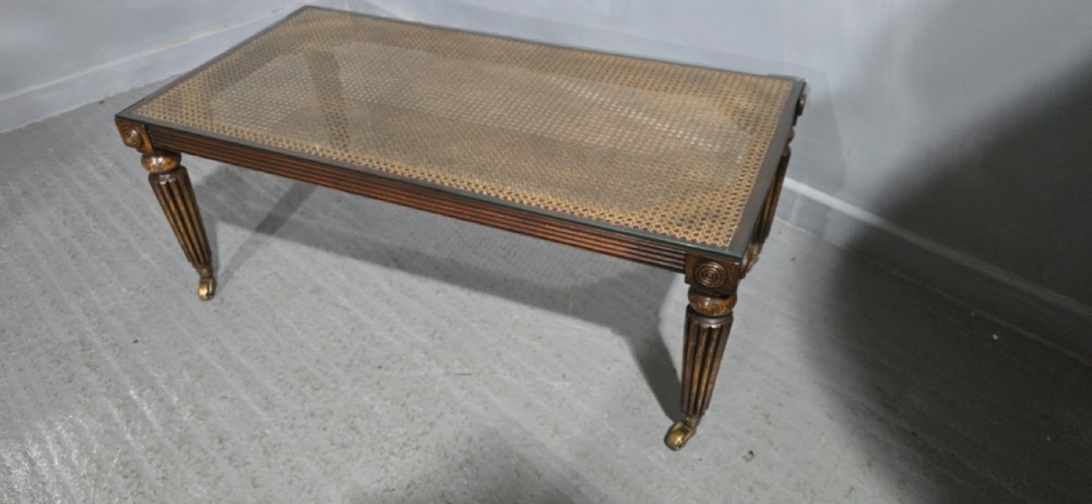 A low rectangular mahogany coffee table featuring a glass-covered woven cane top, reeded frieze, carved corner rosettes, and tapered reeded legs terminating in brass castors. View VI