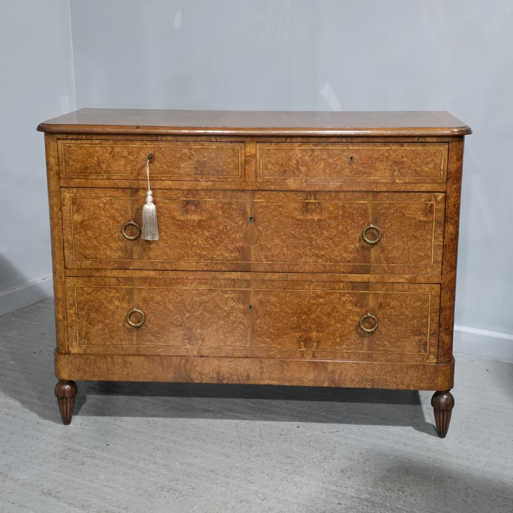 A French amboyna chest of drawers featuring two short drawers over two long drawers, brass ring handles, and turned reeded feet.