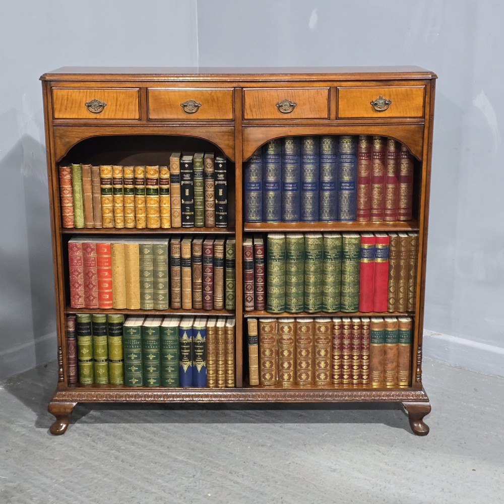 A low warm brown wooden open bookcase featuring four frieze drawers above adjustable shelving sections on carved cabriole feet.