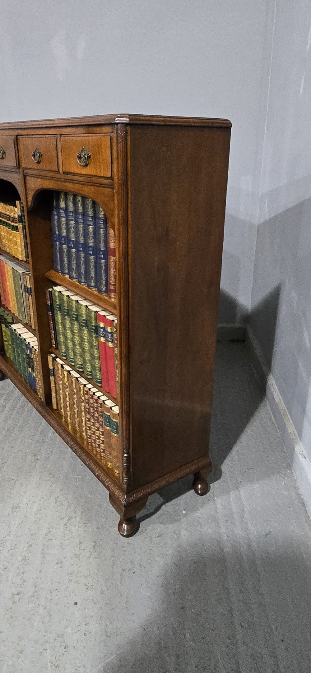A low warm brown wooden open bookcase featuring four frieze drawers above adjustable shelving sections on carved cabriole feet. View VII