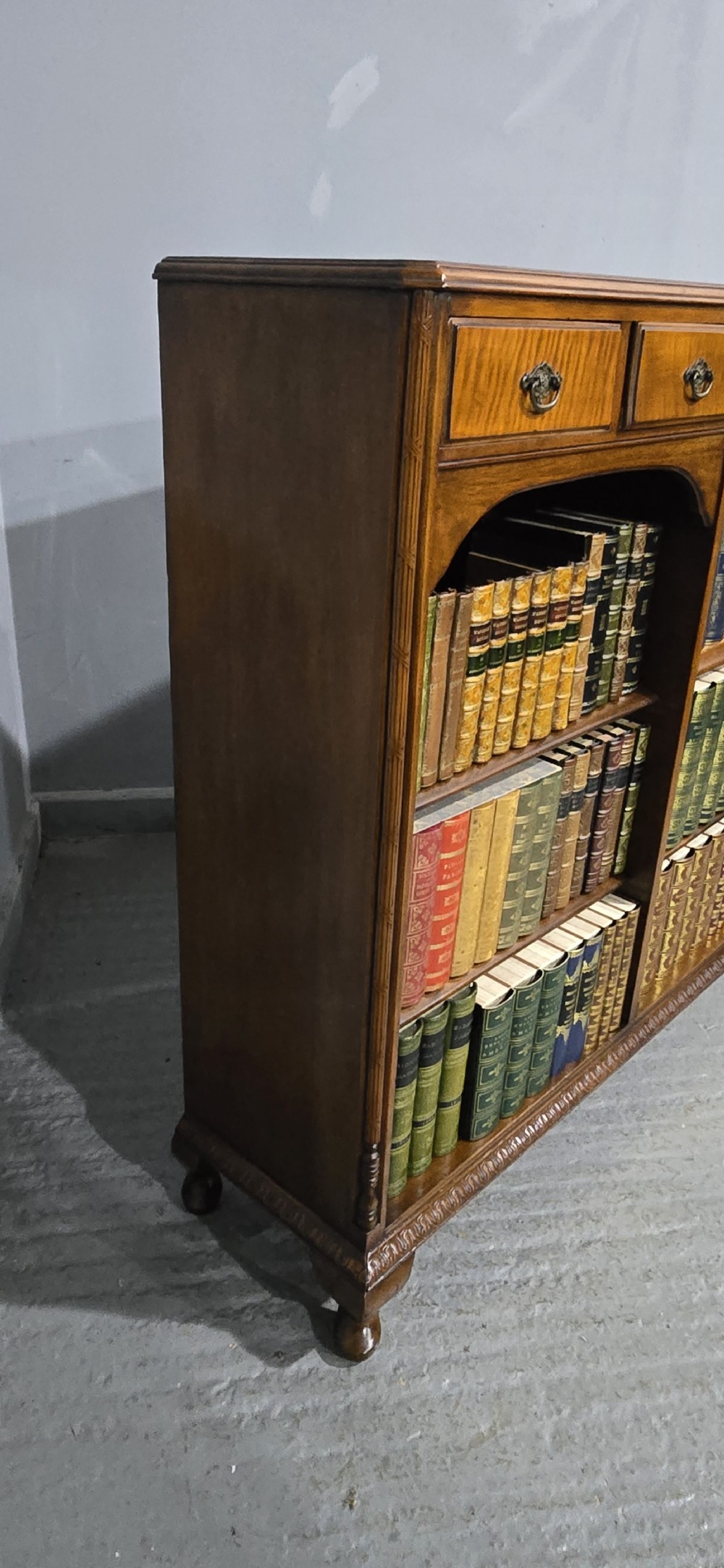 A low warm brown wooden open bookcase featuring four frieze drawers above adjustable shelving sections on carved cabriole feet. View VIII
