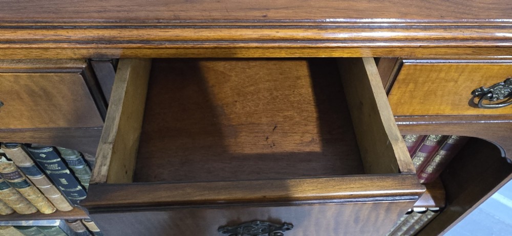 A low warm brown wooden open bookcase featuring four frieze drawers above adjustable shelving sections on carved cabriole feet. View IX
