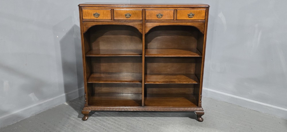 A low warm brown wooden open bookcase featuring four frieze drawers above adjustable shelving sections on carved cabriole feet. View X