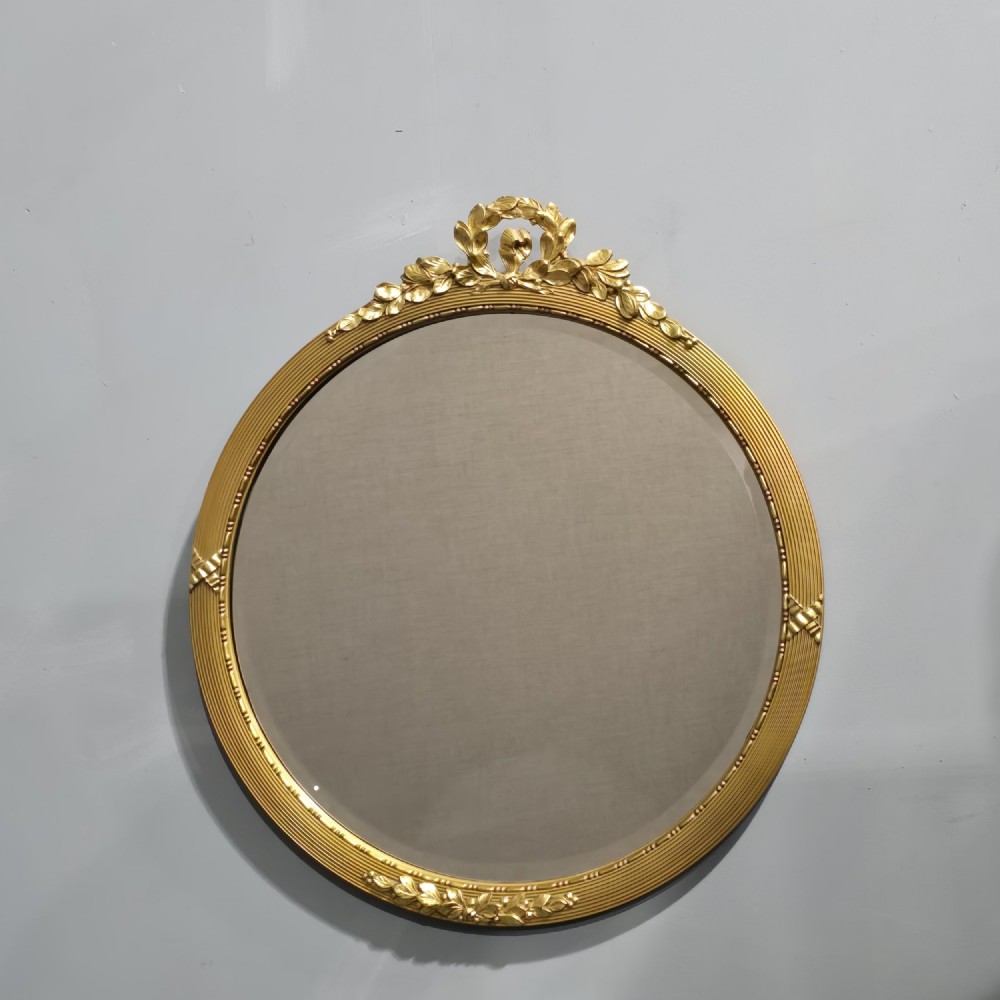 A circular Edwardian gilt mirror featuring a reeded frame topped with an ornate laurel leaf and ribbon crest.