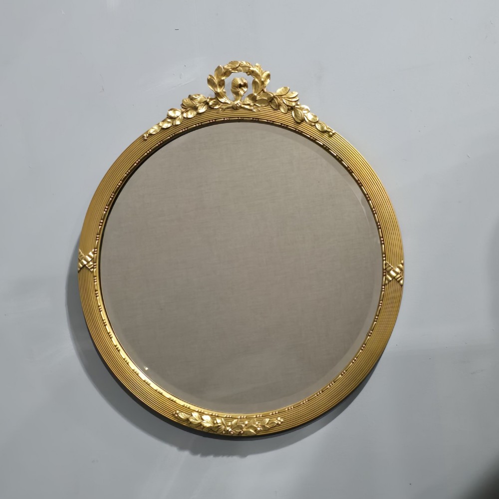 A circular Edwardian gilt mirror featuring a reeded frame topped with an ornate laurel leaf and ribbon crest. View II