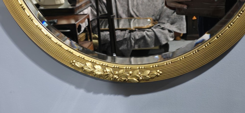 A circular Edwardian gilt mirror featuring a reeded frame topped with an ornate laurel leaf and ribbon crest. View IV