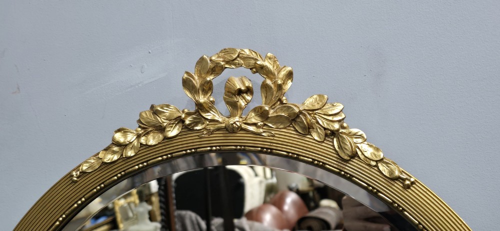 A circular Edwardian gilt mirror featuring a reeded frame topped with an ornate laurel leaf and ribbon crest. View V