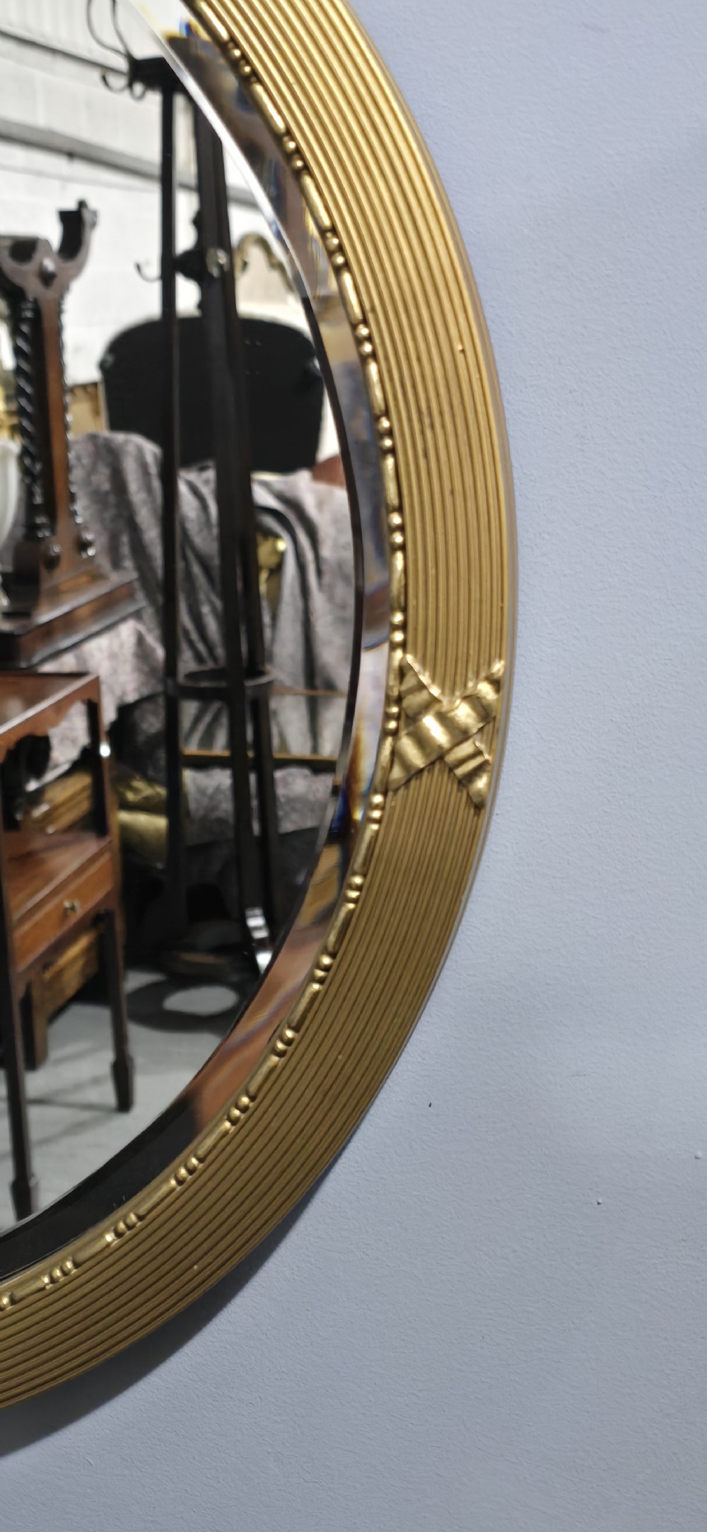 A circular Edwardian gilt mirror featuring a reeded frame topped with an ornate laurel leaf and ribbon crest. View VI