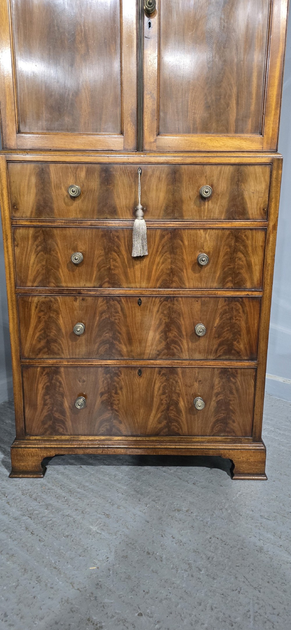 A tall mahogany linen press featuring a double-door upper cupboard with flame mahogany panels over four long drawers with turned knobs. View II