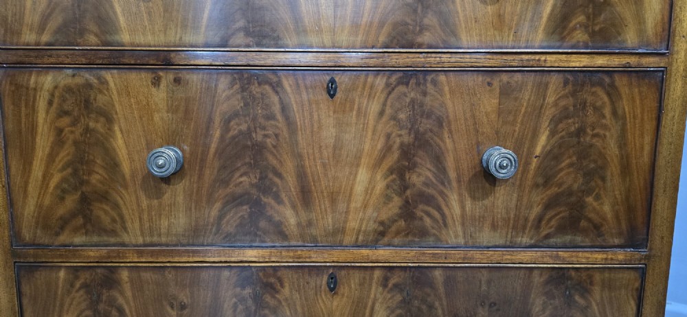 A tall mahogany linen press featuring a double-door upper cupboard with flame mahogany panels over four long drawers with turned knobs. View III