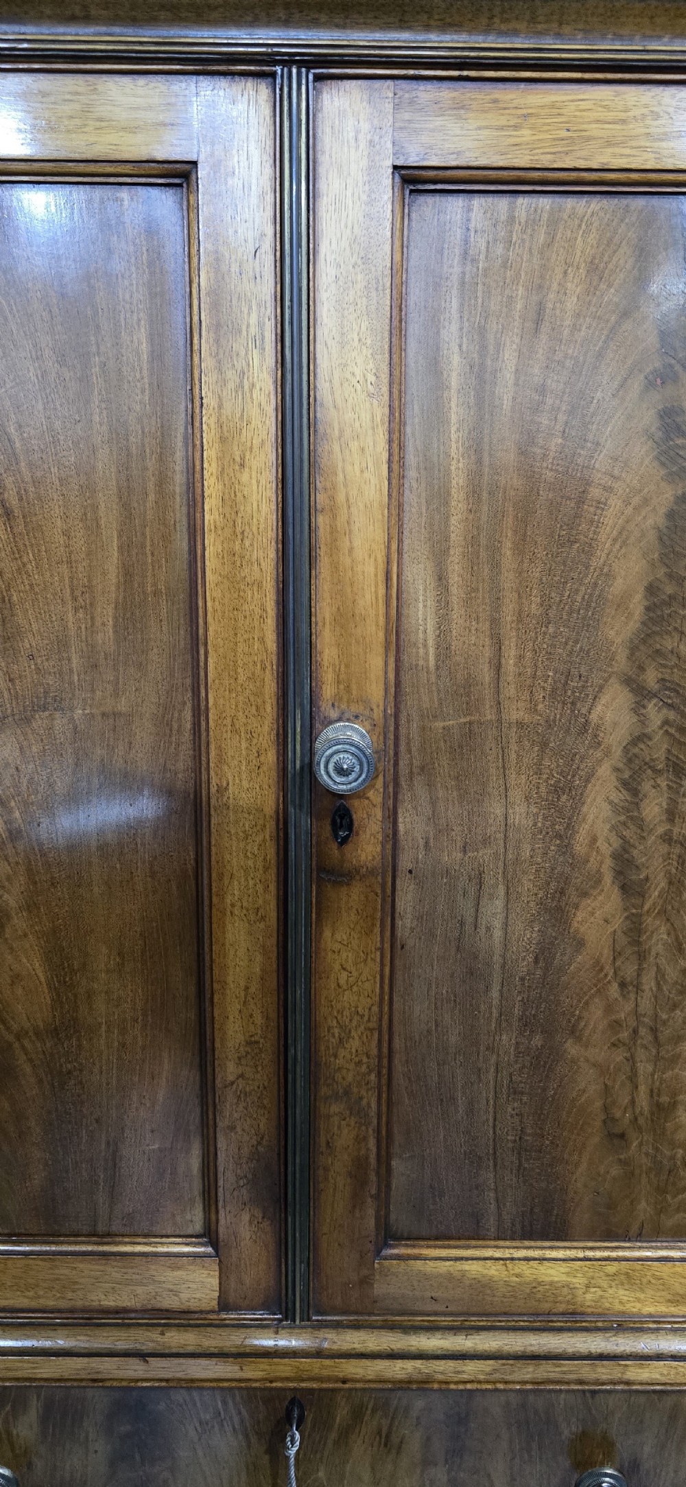 A tall mahogany linen press featuring a double-door upper cupboard with flame mahogany panels over four long drawers with turned knobs. View V