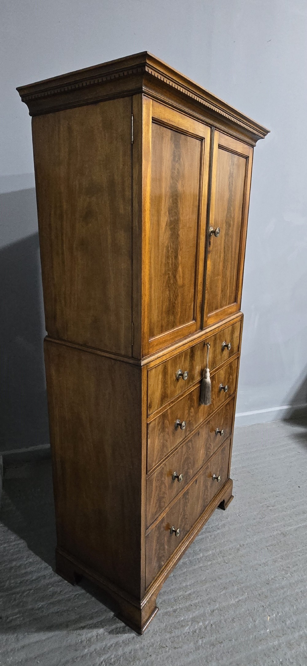 A tall mahogany linen press featuring a double-door upper cupboard with flame mahogany panels over four long drawers with turned knobs. View VII