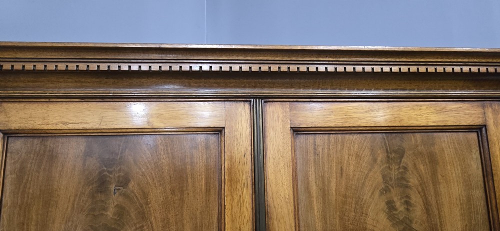 A tall mahogany linen press featuring a double-door upper cupboard with flame mahogany panels over four long drawers with turned knobs. View VIII