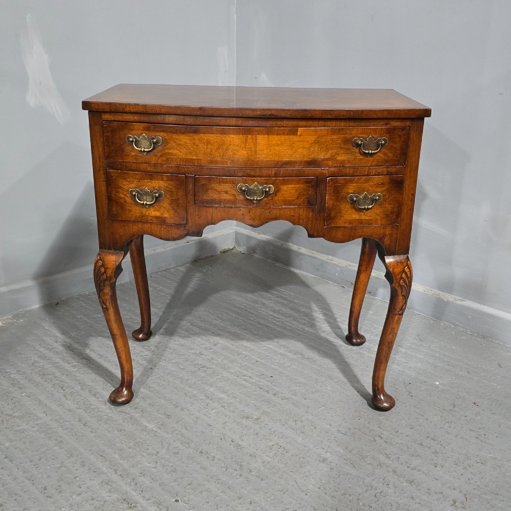 A Queen Anne style burr walnut lowboy table featuring cabriole legs with carved knees, pad feet, brass drop handles, and a shaped apron.