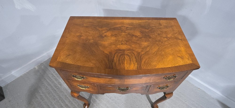 A Queen Anne style burr walnut lowboy table featuring cabriole legs with carved knees, pad feet, brass drop handles, and a shaped apron. View VII