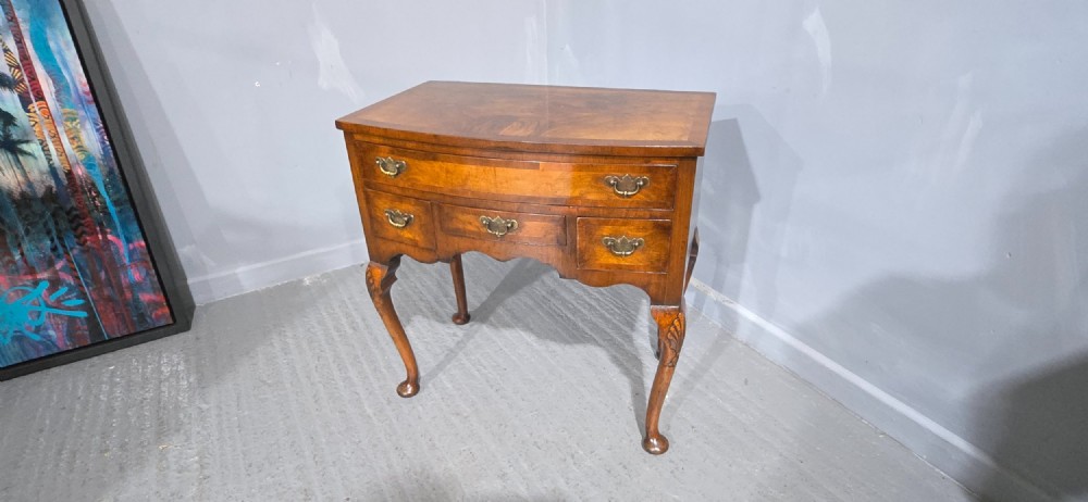 A Queen Anne style burr walnut lowboy table featuring cabriole legs with carved knees, pad feet, brass drop handles, and a shaped apron. View X