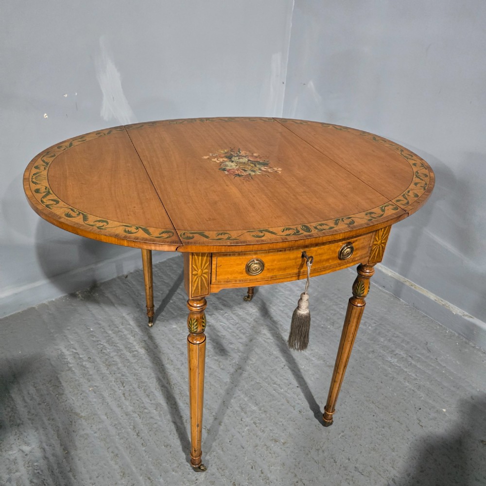 An antique painted satinwood Pembroke table featuring two drop leaves, hand-painted floral borders, turned tapering legs, and a single frieze drawer.