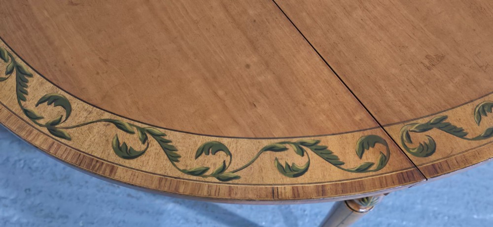 An antique painted satinwood Pembroke table featuring two drop leaves, hand-painted floral borders, turned tapering legs, and a single frieze drawer. View X