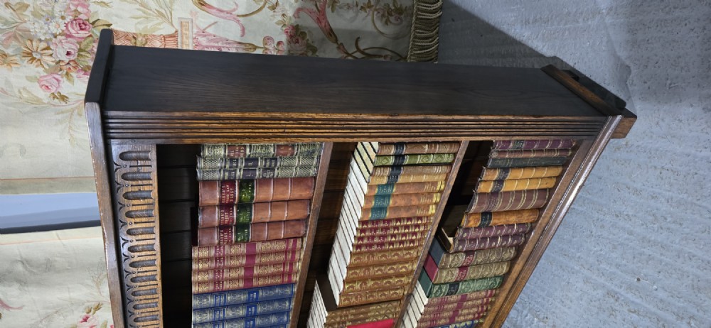 A low solid oak open bookcase with three shelves filled with antiquarian books, featuring a carved arcaded frieze and reeded side moulding. View IV