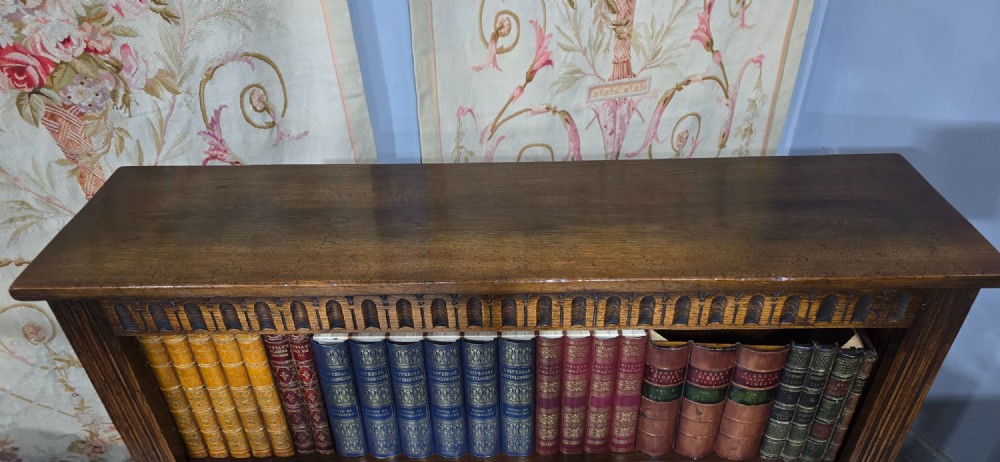 A low solid oak open bookcase with three shelves filled with antiquarian books, featuring a carved arcaded frieze and reeded side moulding. View VI