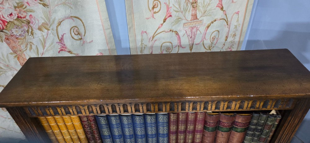 A low solid oak open bookcase with three shelves filled with antiquarian books, featuring a carved arcaded frieze and reeded side moulding. View VII