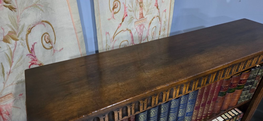 A low solid oak open bookcase with three shelves filled with antiquarian books, featuring a carved arcaded frieze and reeded side moulding. View VIII