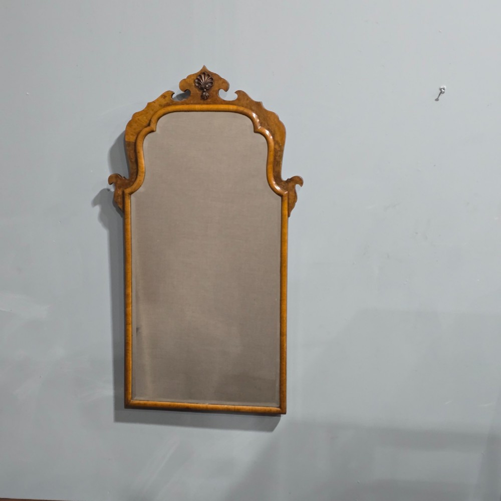 A vertical Queen Anne style wall mirror framed in burr walnut with an arched top and carved shell cresting.