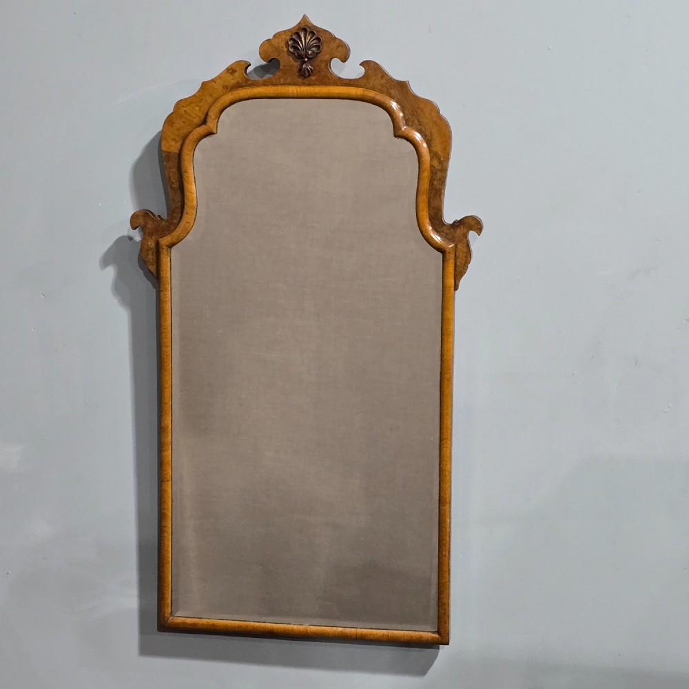 A vertical Queen Anne style wall mirror framed in burr walnut with an arched top and carved shell cresting. View II