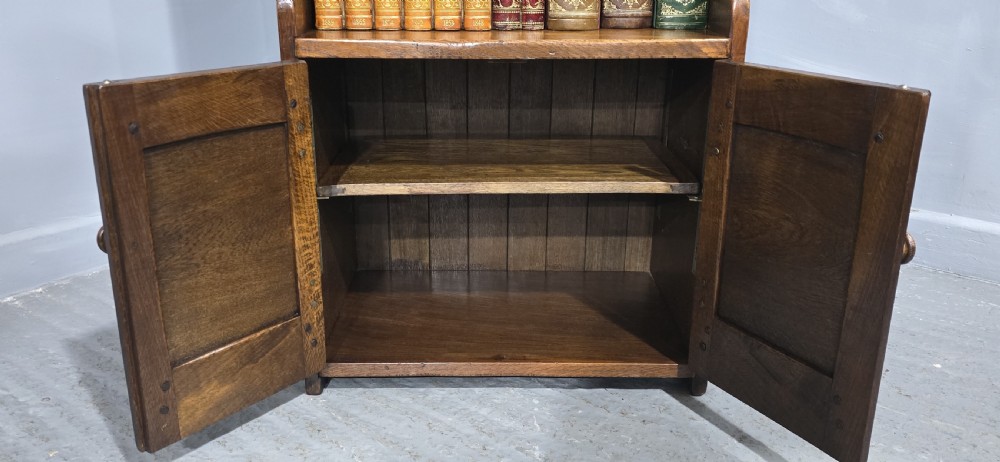 A dark solid oak open bookcase featuring three upper shelves and a two-door base cupboard with carved vertical panels. View V