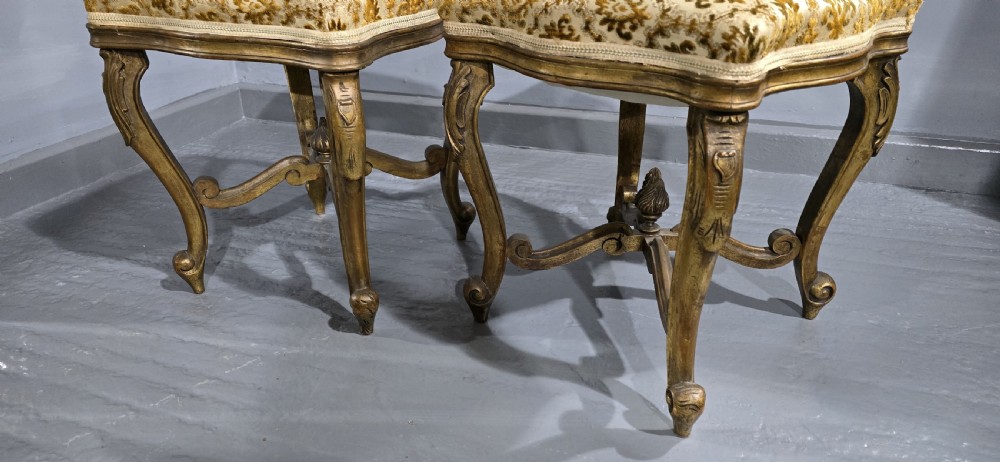 A pair of French giltwood stools featuring patterned gold velvet upholstery, carved cabriole legs, and ornate stretchers. View III