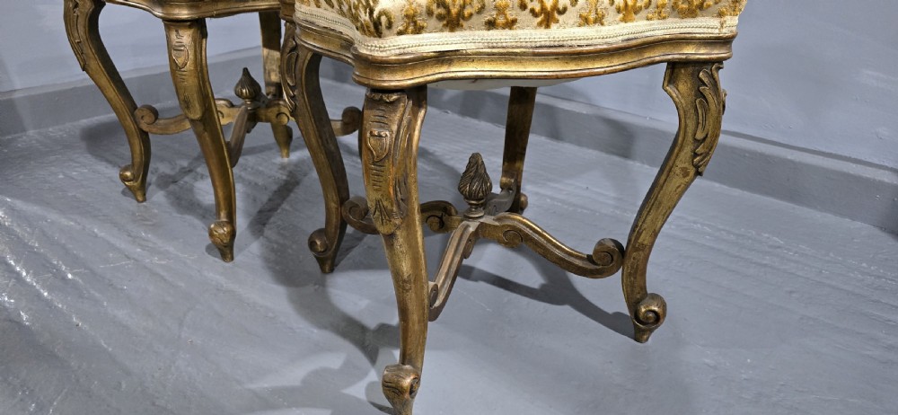 A pair of French giltwood stools featuring patterned gold velvet upholstery, carved cabriole legs, and ornate stretchers. View V
