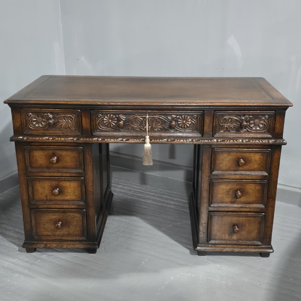 An antique dark oak pedestal desk featuring carved floral frieze drawers, turned wooden knobs, and two pedestals with three drawers each.