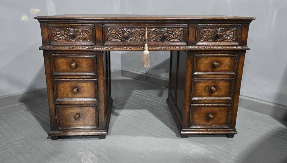An antique dark oak pedestal desk featuring carved floral frieze drawers, turned wooden knobs, and two pedestals with three drawers each. View II